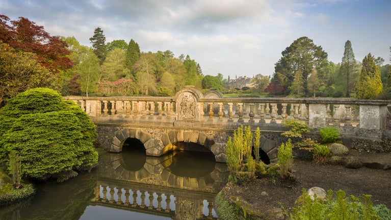 View across the water of First Bridge looking towards the house at Sheffield Park and Garden